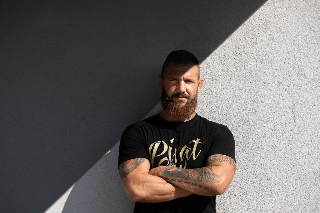 Samuel Krištofič stojí před zdí, má na obličeji stín, na rukou má tetování