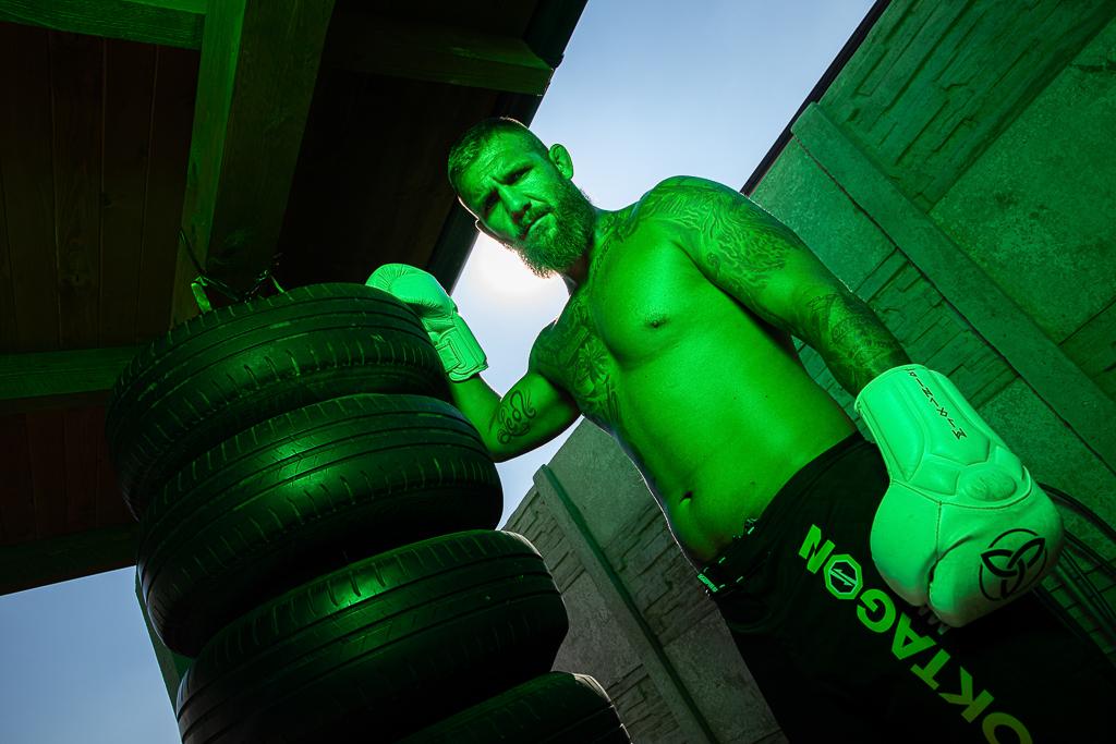 Samuel Krištofič v kraťasech Oktagon, na těle má tetování, na rukou boxovací rukavice, stojí u zavěšených pneumatik
