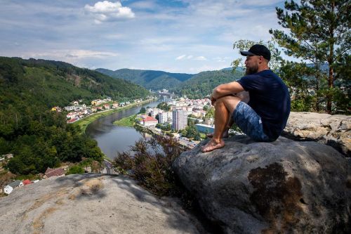 Michal Trávníček sedí na kameni s výhledem na řeku a město