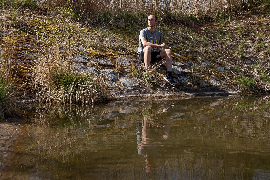 Tomáš Řenč sedí na kamenech u vody v přírodě