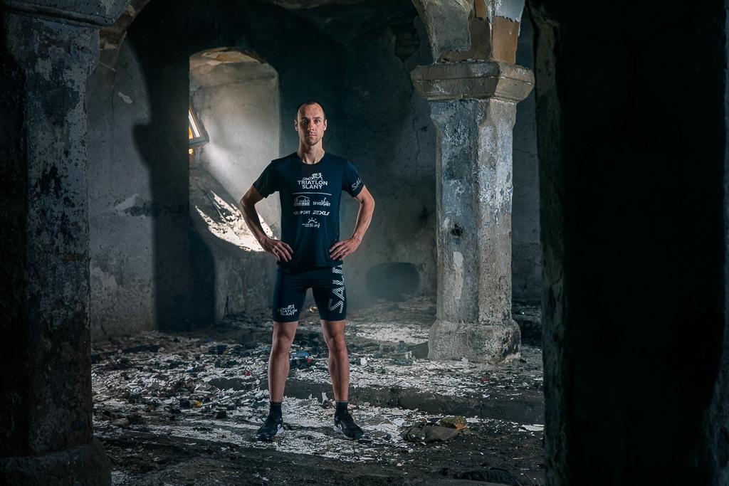 Tomáš Řenč stojí ve starém domě v tričku Triatlon Slaný