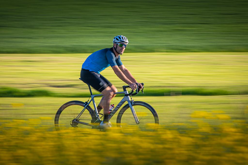 František Raboň jede na kole v cyklistickém dresu a helmě po silnici přírodou