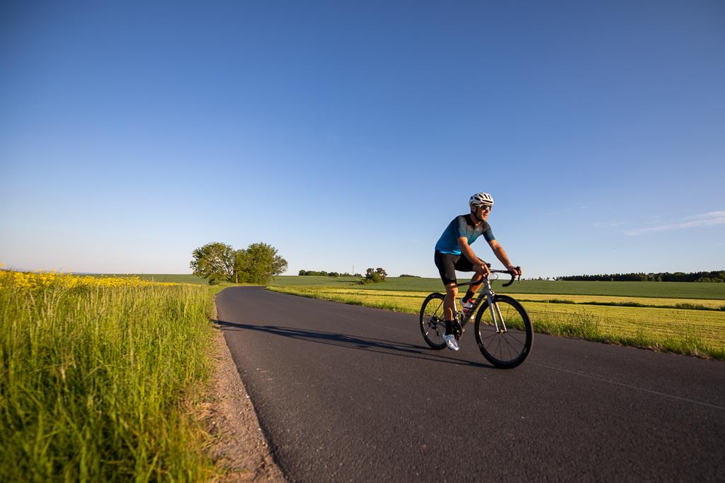František Raboň jede na kole v cyklistickém dresu a helmě po silnici přírodou