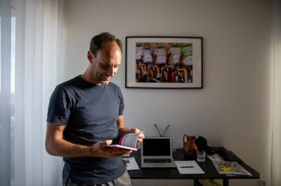 František Raboň listuje v knize, na stole za sebou má notebook, na stěně visí obraz z cyklistického závodu