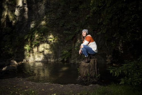 Eva Samková sedí na pařezu u vody a rozhlíží se