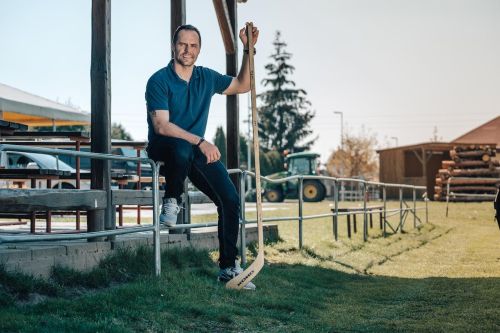 Tomáš Rolinek se opírá o zábradlí na fotbalovém hřišti, drží hokejku s podpisy