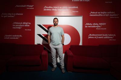 Tomáš Rolinek stojí mezi červenými gauči před zdí s logem Dynama a slogany od jiných sportovců