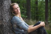 Veronika Zvařičová sedí v lese a opírá se o strom