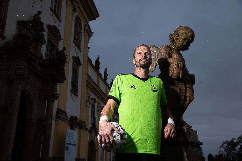 David Rozehnal stojí s fotbalovým míčem pod sochou