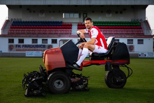 Jan Jeřábek ve fotbalovém oblečení řídí sekačku na trávu na stadionu