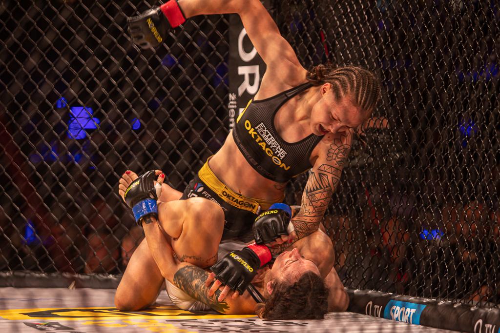 Tereza Bledá má napřaženou ruku nad soupeřkou v kleci při zápase MMA
