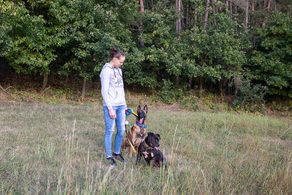 Tereza Bledá stojí na louce s dvěma psy, za nimi je les