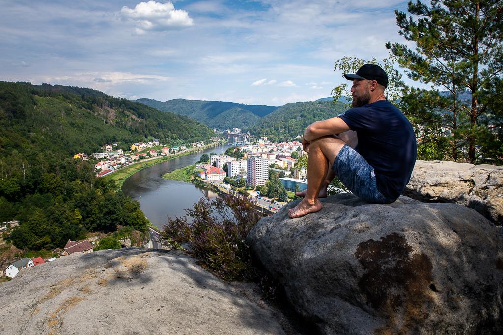 Michal Trávníček sedí na kameni s výhledem na řeku a město