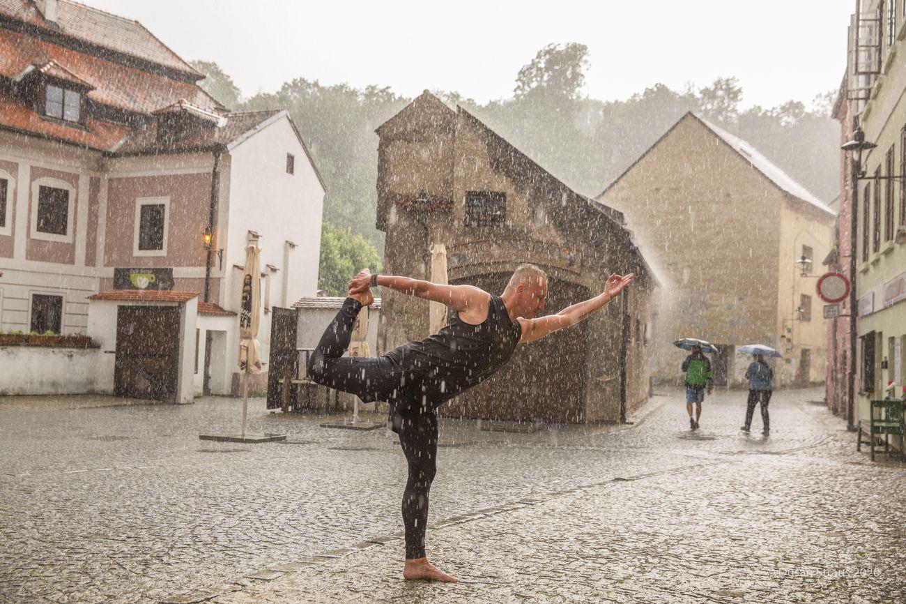 Václav Krejčík v jógové póze ve městě na kostkách v dešti