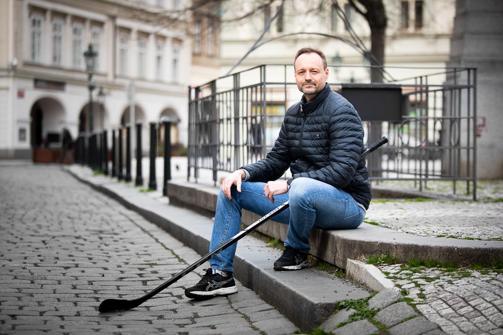 Petr Míka sedí na schodech na kostkách ve městě s hokejkou