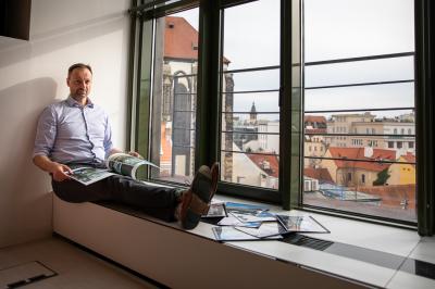 Petr Míka sedí u okna s výheldem na město, prohlíží si katalogy