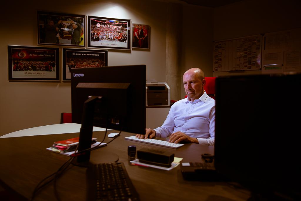 Jan Peterek sedí u stolu a kouká do počítače, na stěne visí obrazy HC Oceláři Třinec