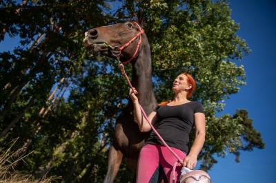 Barbora Miksánková Málková se prochází vedle koně v přírodě, v ruce drží helmu
