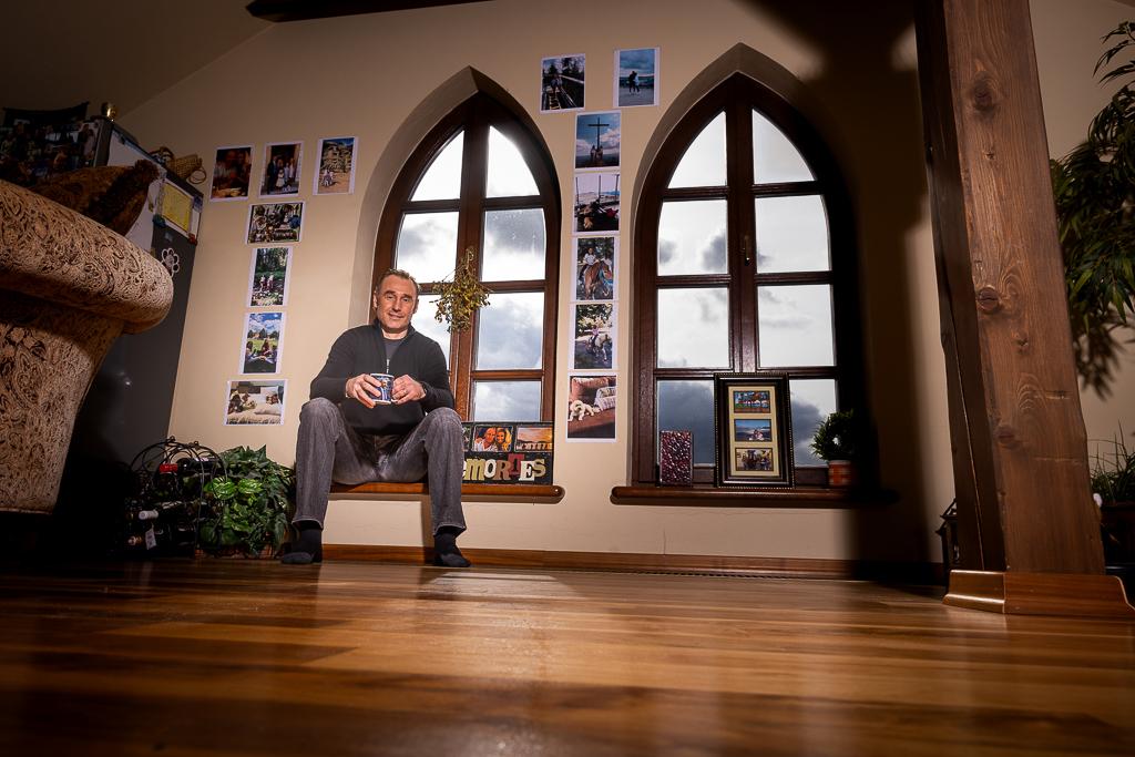 Václav Propsal sedí na parapetu okna, nad ním visí jeho zarámované fotografie.