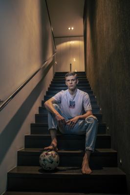 Jegor Cykalo sedí na osvětlených schodech s fotbalovým míčem.