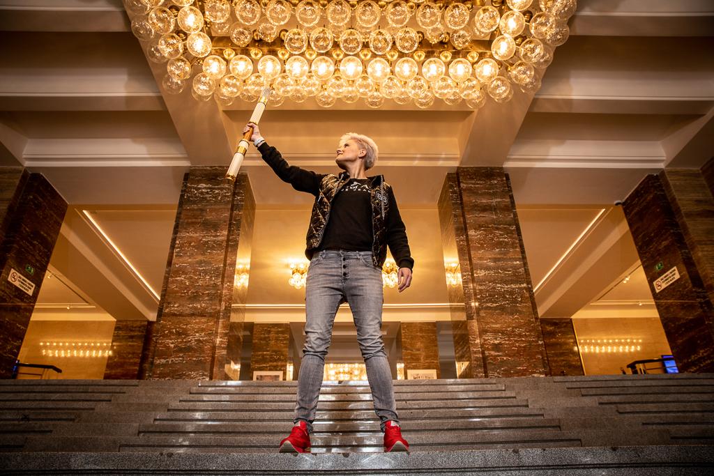 Markéta Pernická drží pochodeň stojí na schodech v budově pod velkým lustrem