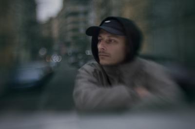 Rozostřená fotografie Tomáše Kučery opřeného o automobil.
