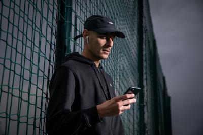 Tomáš Kučera opřený o sportovní síť hledí do mobilu