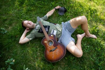 Marek Mazanec leží v trávě, má u sebe kytaru