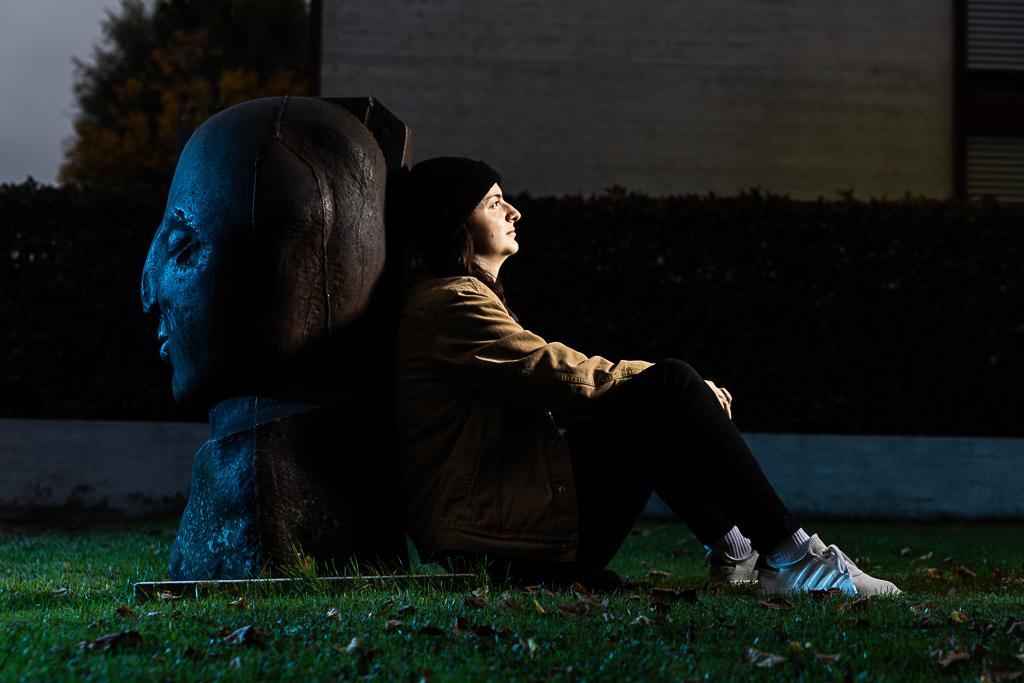 Natálie Martináková sedí na trávníku a zády se opírá o sochu.