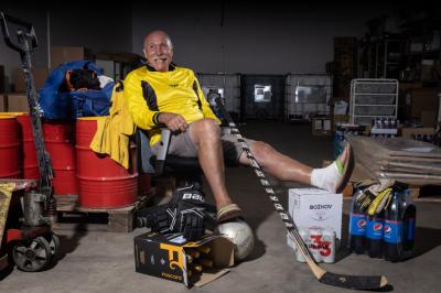 Evžen Musil sedí na jezdící židli ve skladu, má u sebe hokejové rukavice, hokejku, kolem jsou nápoje, palety, paleťák