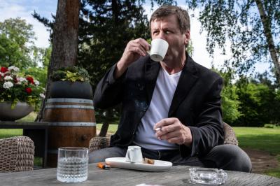 Otakar Janecký pije kafe, v ruce má cogaretu, sedí u stolku v parku