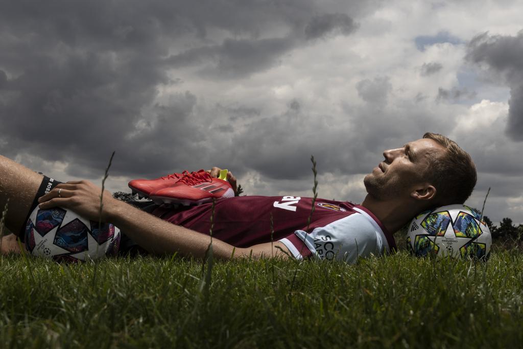 Tomáš Souček leží na trávníku, pod hlavou má fotbalový míč.