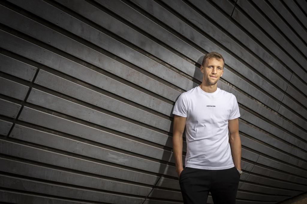 Tomáš Souček stojí v tričku před dřevěnou zdí, jednu ruku má v kapse.