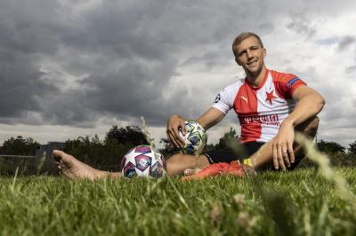Tomáš Souček sedí bosí na trávníku, v ruce má fotbalový míč.