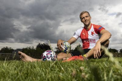 Tomáš Souček sedí bosí na trávníku, v ruce má fotbalový míč.