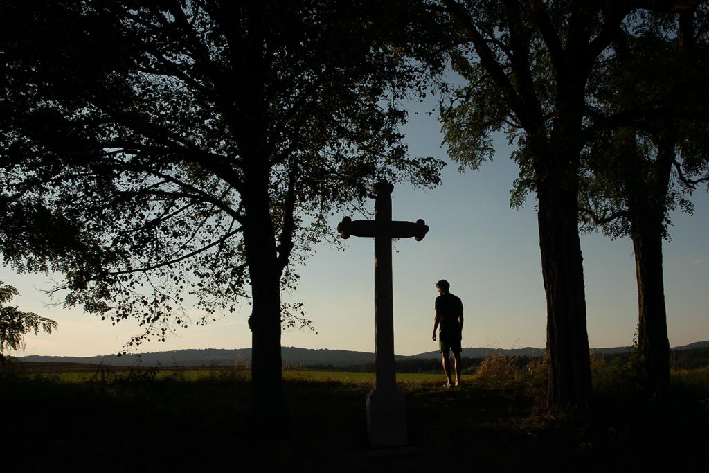 Aleš Matějů stojí před polem, za ním je kamenný kříž