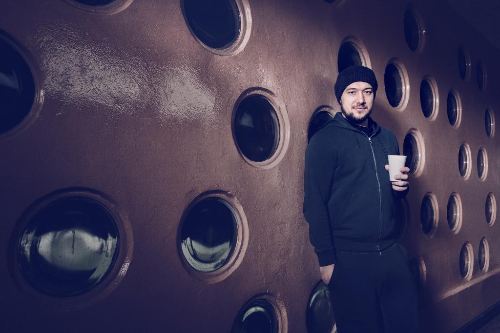 Jan Kovář stojí opřený o uměleckou zed' a drží v ruce kafe
