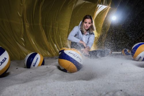 Markéta Sluková sedí na písku s volejbalovými míči.