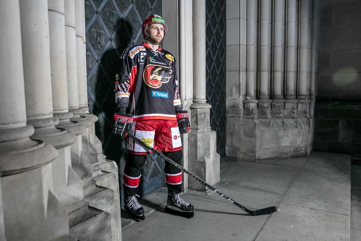 Matouš Maxmilián Venkrbec stojí v hokejovém dresu před branami kostela.