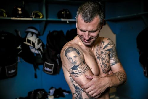 Michal Broš stojí odhalený v kabině, ukazuje své tetování na paži.