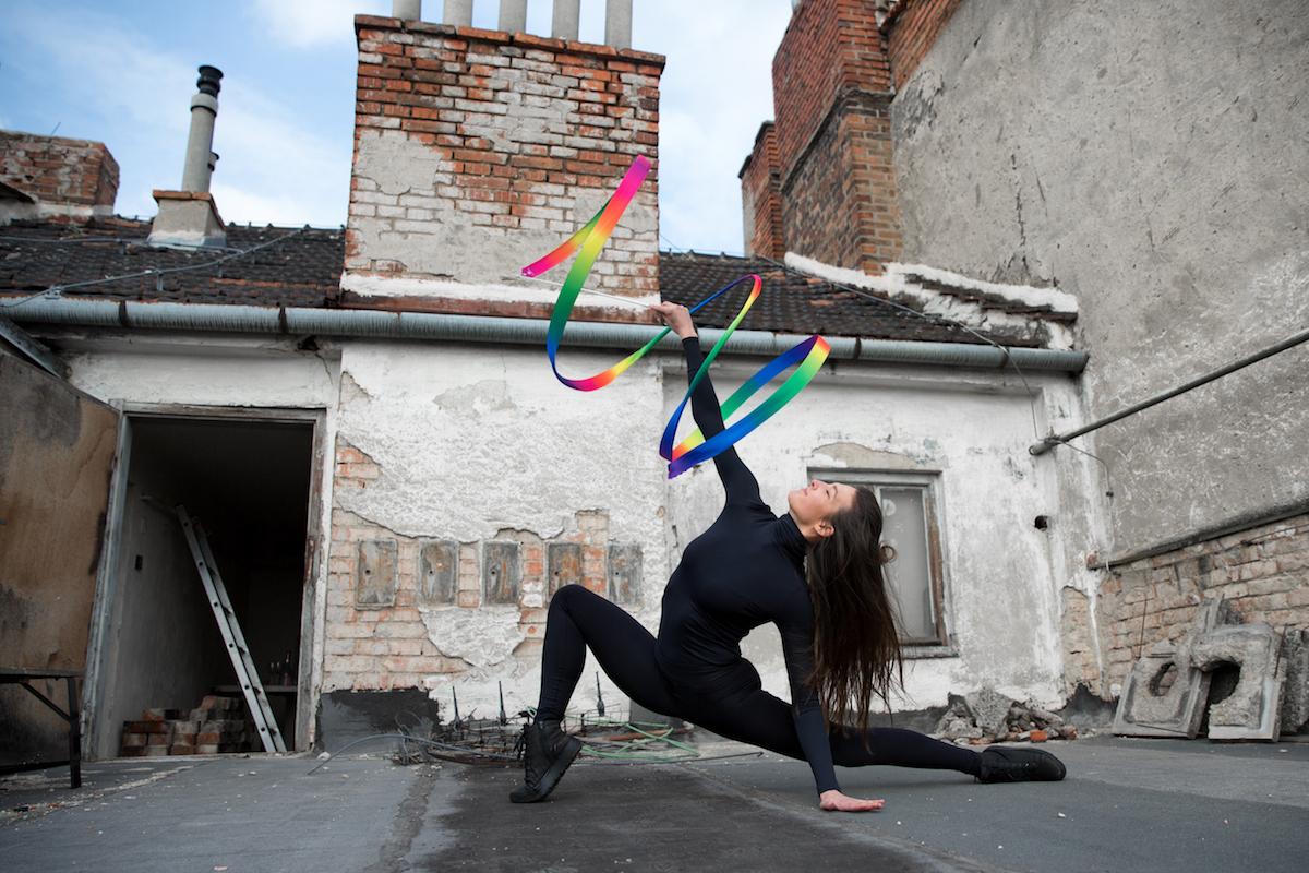 Monika Míčková cvičí s barevnou stuhou na střeše domu.