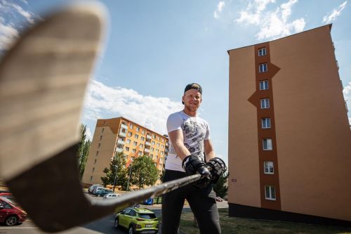 Ondřej Kaše s hokejkou v ruce stojí před paneláky, kde vyrostl.