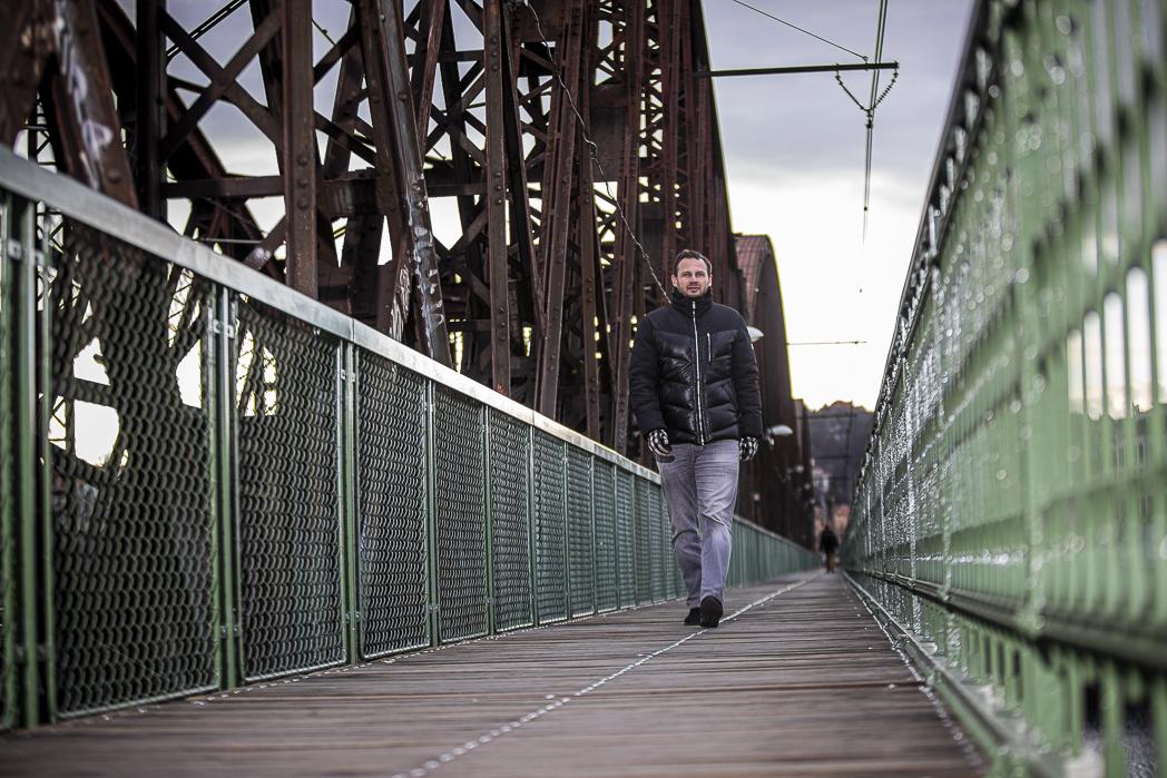 Pavel Brendl jde po pražském železničním mostě.