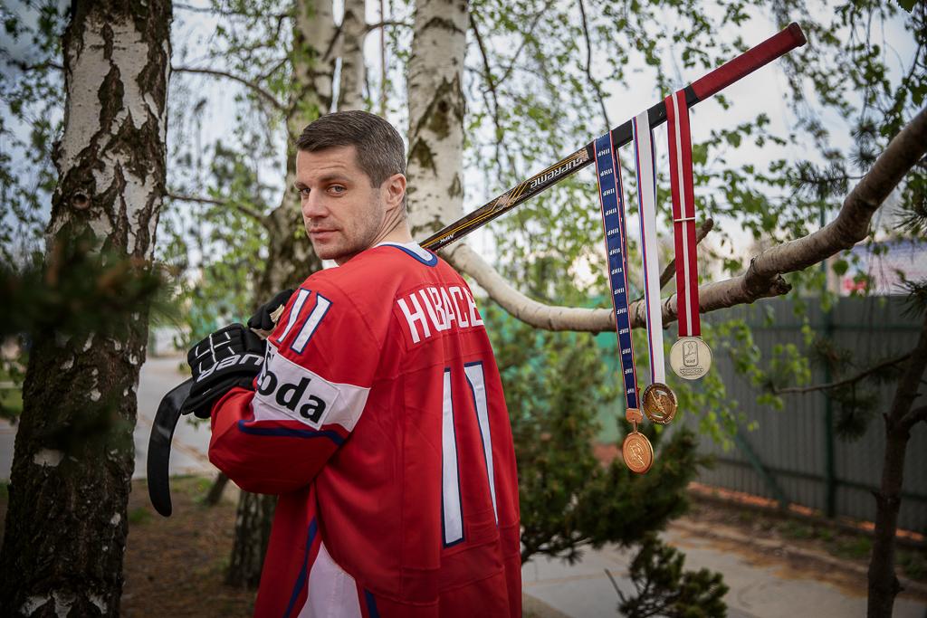 Petr Hubáček v národním hokejovém dresu nese hokejky a na ní medaile.