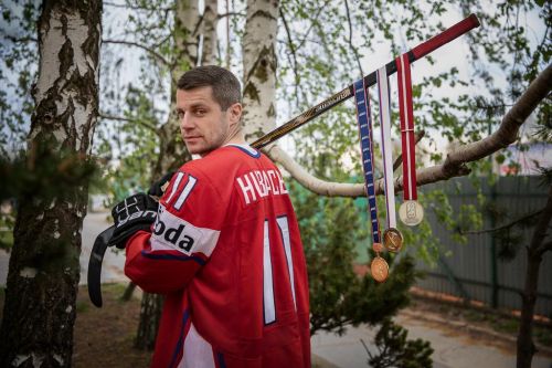 Petr Hubáček v národním hokejovém dresu nese hokejky a na ní medaile.