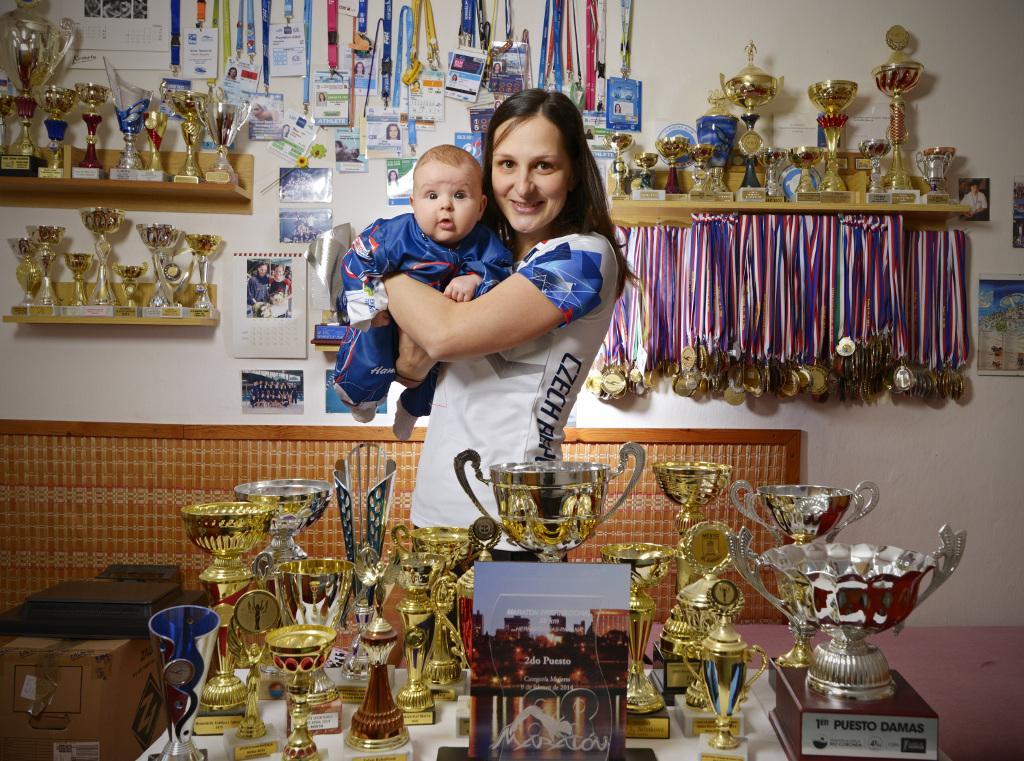 Silvie Kodešová s miminkem mezi svými medailemi a trofejemi.